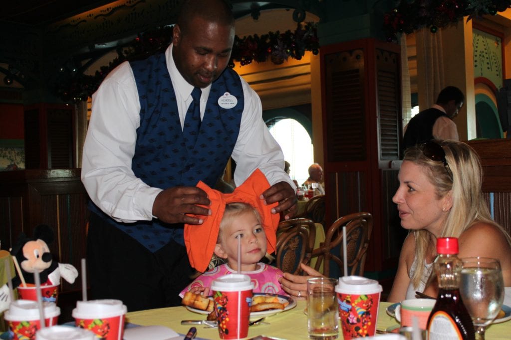 Waiter making a big Minnie Bow for little girl at dining table onboard Disney Cruise Line | Global Munchkins